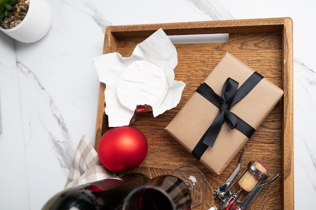 Kerstdiner geserveerd op houten dienblad. Wijn, kaas, kerstballen en een ingepakt cadeau, bovenaanzicht. Hoge kwaliteit foto