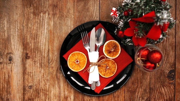 Kerstdinerdecoratie met gedroogde sinaasappelen en een rood servet op een zwarte plaat. kunstkerstboom op houten achtergrond