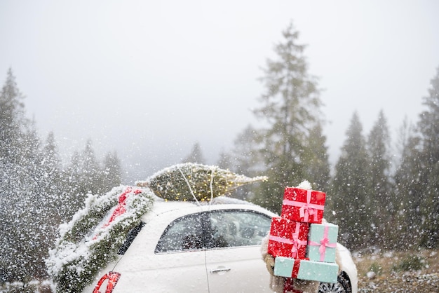 Kerstfotokaart van een vrouw met cadeautjes en auto in de bergen bij sneeuwweer