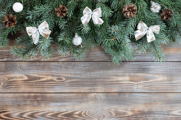 Kerstgrens met dennentakken, zilveren ballen en strikken, kegels op een houten achtergrond.