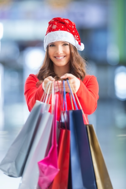 Kerstinkopen doen. Aantrekkelijk gelukkig meisje met creditcard en boodschappentassen in kerstmuts.