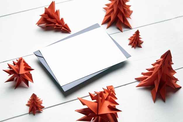 Foto kerstkaart mockup met envelop en rode papieren sparren op witte houten achtergrond close-up