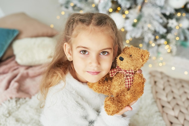 Kerstkind op de achtergrond van de kerstboom met speelgoedteddybeer.