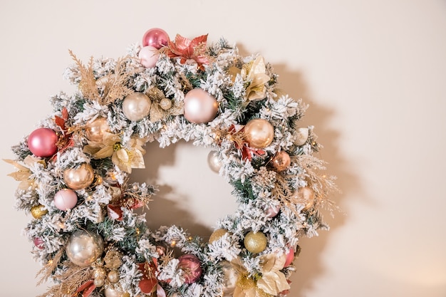 Kerstkrans gemaakt van natuurlijke fir takken opknoping op een beige muur.