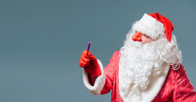 Kerstman blauwe studio achtergrond in rode dop witte baard kijk naar de camera wijs naar de andere kant met de aanwijzer