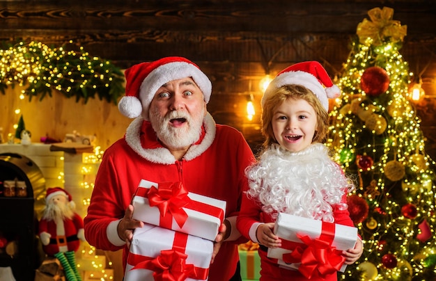 Kerstman en kindjongen in kamer versierd voor kerstmis met huidige geschenkdoos wintervakantie