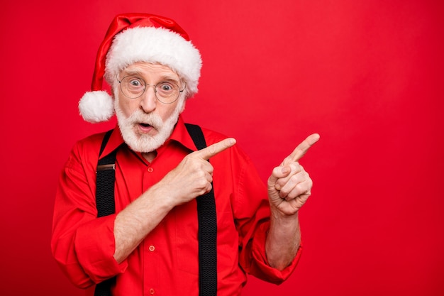 Kerstman in bretels en hoed poseren op rode muur