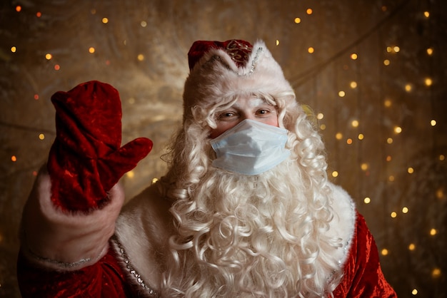 Kerstman in een medisch masker op een muurachtergrond met bokeh van slingers