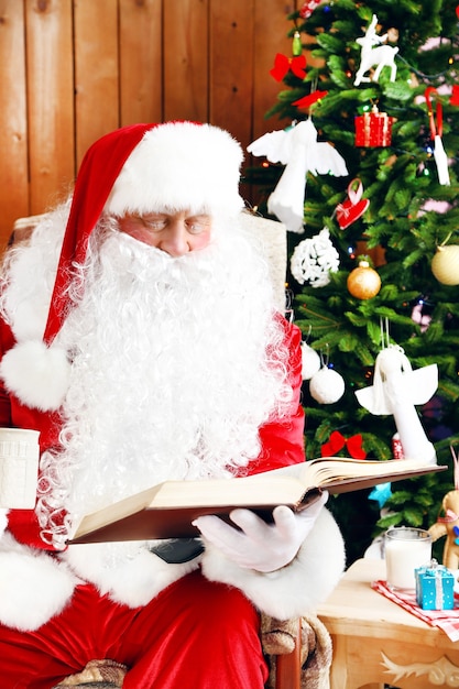 Kerstman met boek zittend in comfortabele schommelstoel in de buurt van Kerstmis thuis