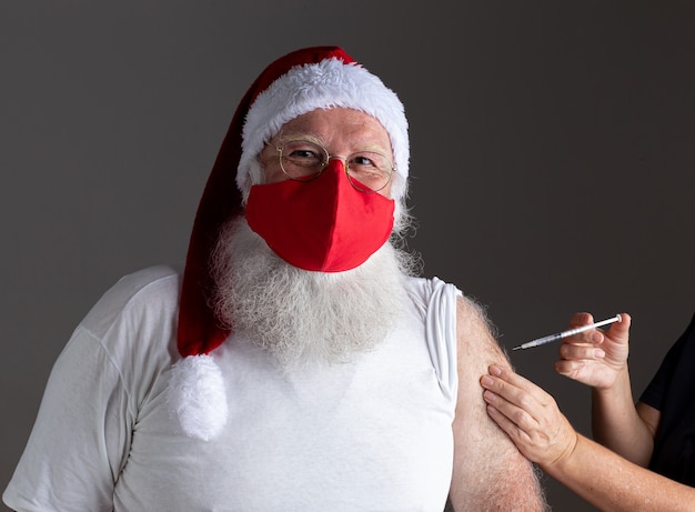 Kerstman met gezichtsmasker wordt gevaccineerd met injectie