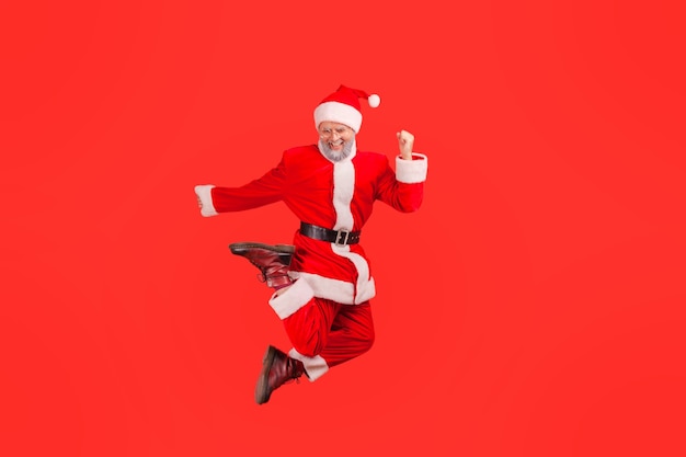 Kerstman springt naar de lucht met een blije opgewonden uitdrukking en viert wintervakanties.