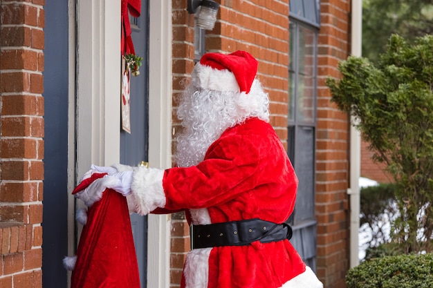 Kerstman van het dragen van een kerstcadeau levering van een grote zak buitenshuis, in de buurt van huis