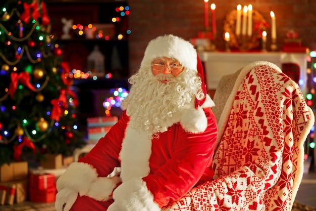 Kerstman zittend in een comfortabele stoel bij de open haard thuis