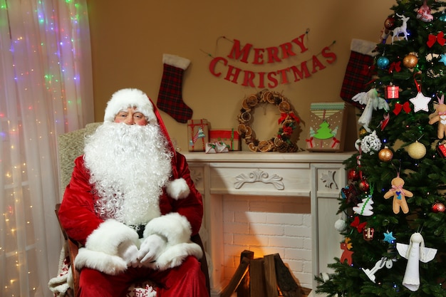 Kerstman zittend in een comfortabele stoel bij de open haard thuis