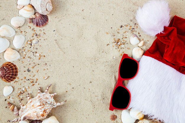 Kerstmanhoed en oogglazen op het zand dichtbij shells. Holiday. Nieuwjaars vakantie.