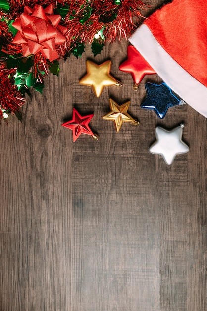 Kerstmanhoed met metaalsterren, ornament en rood lint op houten achtergrond.