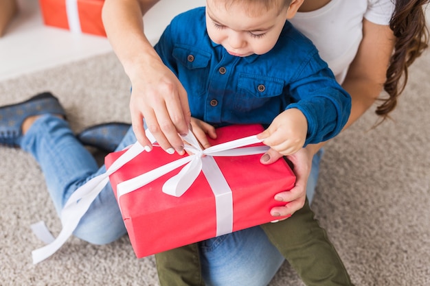 Kerstmis, alleenstaande ouder en vakantie concept - Close-up van schattige kleine jongen die kerstcadeau voor zijn moeder thuis vasthoudt.