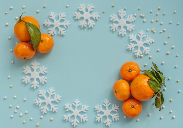 Kerstmis blauwe achtergrond met oranje mandarijnen en witte sneeuwvlokken. Nieuwjaar wenskaart. Plat lag stijl.