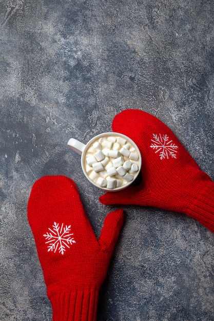 Kerstmis en Nieuwjaar gezellige vakantie samenstelling met sjaal, vrouw handen wanten, mokken met warme drank en marshmallow op de grijze concrete achtergrond in. Plat lag, bovenaanzicht.