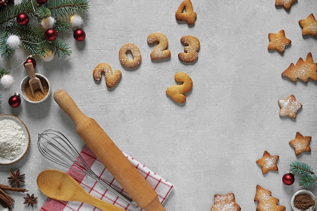 Kerstmis en Nieuwjaar samenstelling van cookies nummers 2023 en sterren op betonnen achtergrond en keukengerei bovenaanzicht kopieerruimte