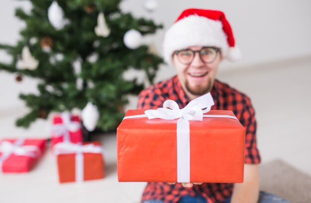 Kerstmis en vakantie concept - grappige man in kerstmuts met een cadeau thuis in de woonkamer.