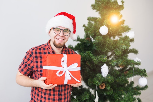 Kerstmis en vakantie concept - grappige man in kerstmuts met een cadeau thuis in de woonkamer.