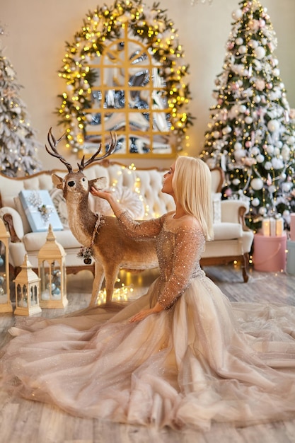 Kerstmis, feest en mensen concept - jonge vrouw in elegante jurk over fairy christmas interieur achtergrond.