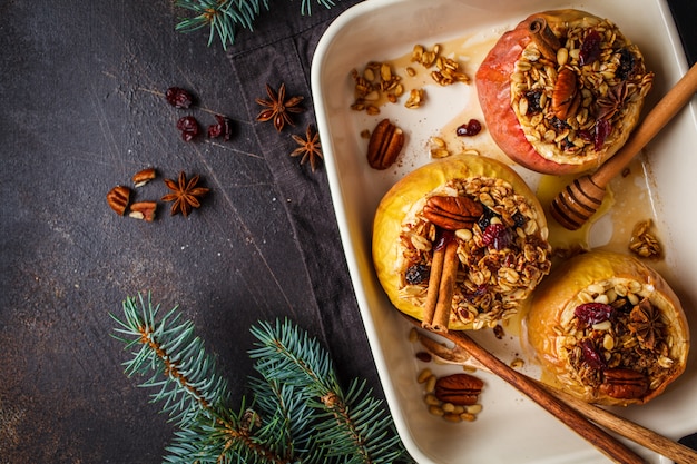 Kerstmis gebakken appelen met granola, amerikaanse veenbessen, noten en honing in de ovenschotel, donkere achtergrond.