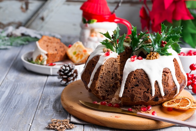 Kerstmis gesneden chocoladecake met wit suikerglazuur, hulsttakken en granaatappelpitten een grijze houten