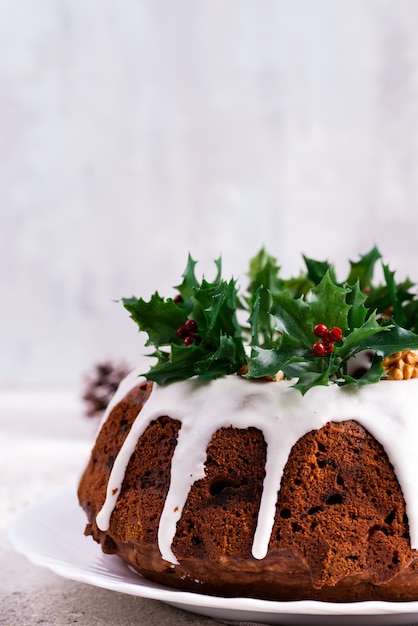 Kerstmis homebaked donkere chocolade bundt cake die met het witte suikerglazuur en hulstbessentakkenclose-up wordt verfraaid