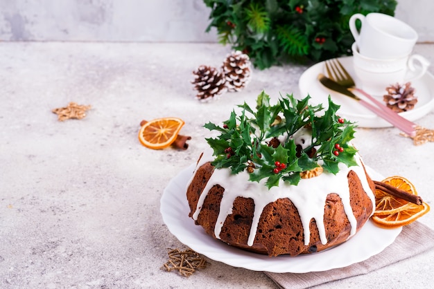 Kerstmis homebaked donkere chocolade bundt cake die met het witte suikerglazuur en hulstbessentakkenclose-up wordt verfraaid