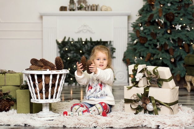 Kerstmis is hier. Meisjespelen met denneappelsdecoratie aan de Kerstboom. Dozen met geschenken staan op de vloer. Kerstmis vieren.