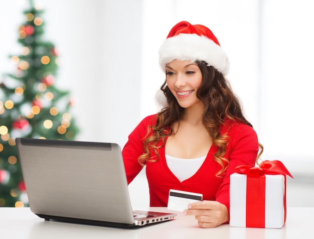 Kerstmis, Kerstmis, online winkelconcept - vrouw in kerstmuts met geschenkdoos, laptopcomputer en creditcard