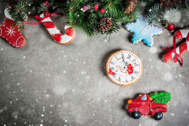 Kerstmis met sparrentak, zelfgemaakte kleurrijke peperkoekkoekjes, dennenappels en decoraties op grijze stenen tafel. Bovenaanzicht, copyspace