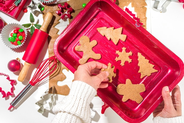 Kerstmis, Nieuwjaar koken achtergrond. Bakken ingrediënten en gebruiksvoorwerpen - peperkoek deeg, koekjes uitstekers, deegroller. Vrouw handen maken feestelijke kerst zoete koekjes helder feestelijk rood wit concept