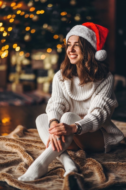 Kerstmis, nieuwjaar. Mooie vrouw in warme trui, sokken en kerstmuts, zittend op de vloer