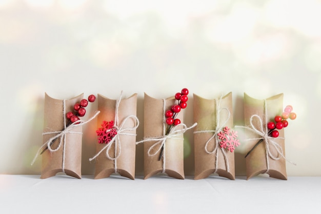 Foto kerstmis, nieuwjaar wenskaart met ambachtelijke papier geschenkdozen met packthres bogen en rode decoratieve bessen en rode sneeuwvlokken op witte achtergrond.