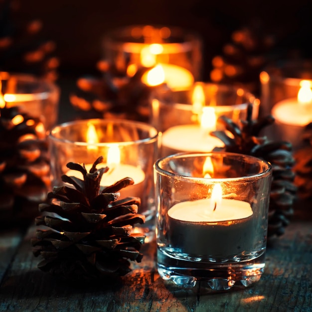 Kerstmis of Nieuwjaar compositie met brandende kaarsen in kleine glazen kandelaars en dennenappels vintage houten achtergrond feestelijke avond selectieve focus