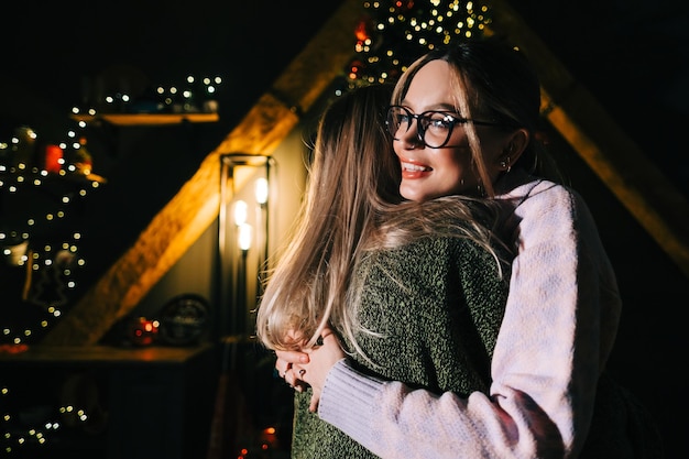 Kerstmis of nieuwjaarsviering, twee jonge gelukkige vrouwen omhelzen elkaar in de buurt van de kerstboom.