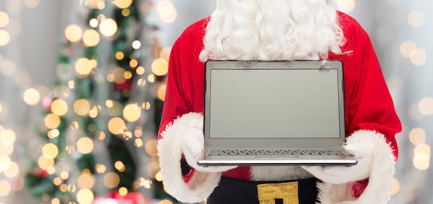 Kerstmis, reclame, technologie en mensenconcept - close-up van de kerstman met laptopcomputer over de achtergrond van boomlichten