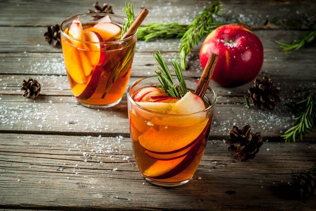 Kerstmis, thanksgiving-drankjes. herfst, wintercocktail, warme sangria, glühwein - appel, rozemarijn, kaneel, anijs. op oude rustieke houten tafel. met kegels, rozemarijntakken. kopieer ruimte