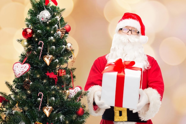 Kerstmis, vakantie en mensen concept - man in kostuum van de kerstman met geschenkdoos en boom over beige lichten achtergrond