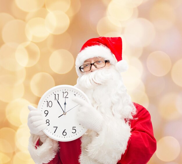 Kerstmis, vakantie en mensenconcept - man in kostuum van de kerstman met klok die twaalf toont over beige lichtenachtergrond