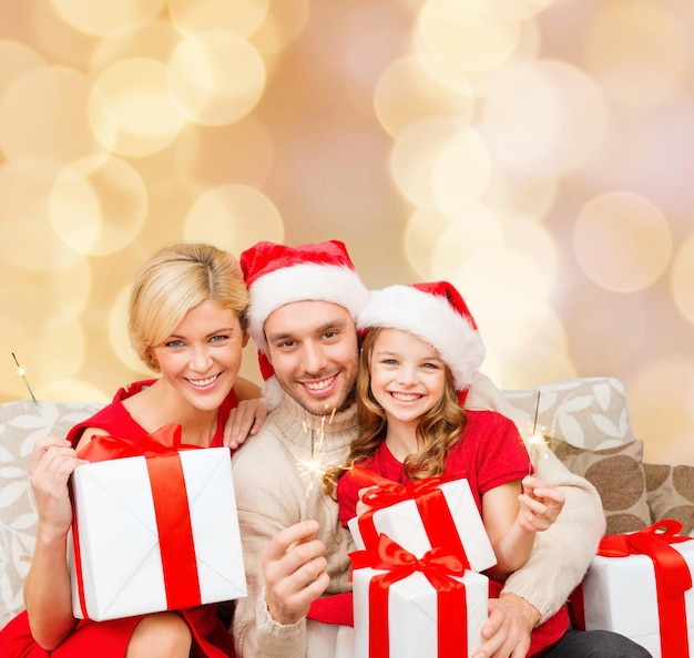 Kerstmis, vakantie, familie en mensen concept - gelukkige moeder, vader en klein meisje in santa helper hoeden met geschenkdozen en sterretjes over beige lichten achtergrond