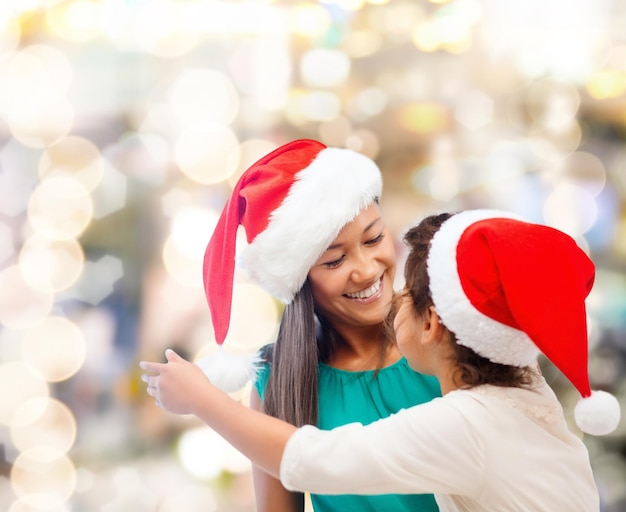 Kerstmis, vakantie, feest, familie en mensen concept - gelukkige moeder en klein meisje in santa helper hoeden over lichten achtergrond