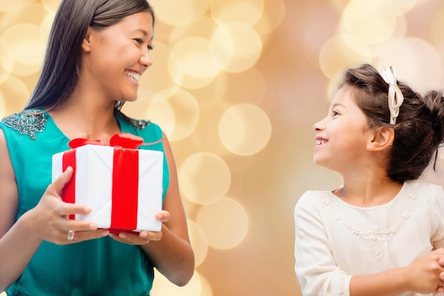 Kerstmis, vakantie, feest, familie en mensen concept - gelukkige moeder en meisje met geschenkdoos over beige lichten achtergrond