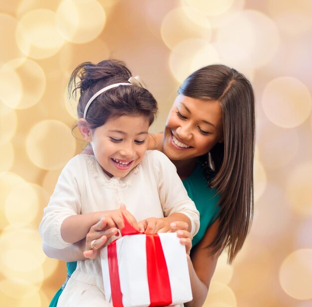 Kerstmis, vakantie, feest, familie en mensen concept - gelukkige moeder en meisje met geschenkdoos over beige lichten achtergrond