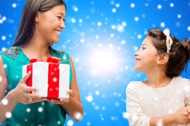Kerstmis, vakantie, feest, familie en mensen concept - gelukkige moeder en meisje met geschenkdoos over blauwe besneeuwde achtergrond