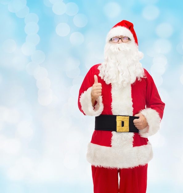 Kerstmis, vakantie, gebaar en mensen concept-man in kostuum van de kerstman duimen opdagen over blauwe lichten achtergrond
