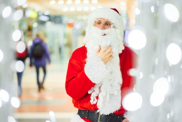 Kerstmis, vakantie, gebaar en mensenconcept - man in kostuum van de kerstman die over de achtergrond van het winkelcentrum zwaait